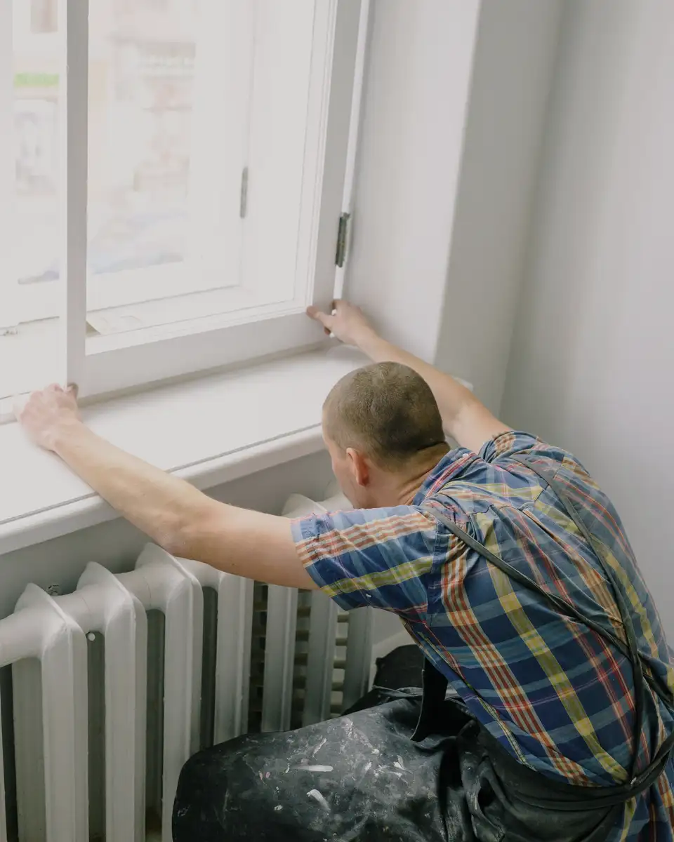 An installer setting a new window into a frame above a radiator